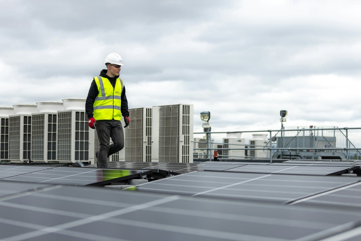 Technik kontroluje solárne panely a jednotky HVAC na streche komerčnej budovy.